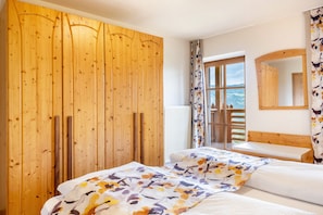 A bedroom with a wooden wardrobe, a bed with floral bedding, a window with a view, and a wooden headboard.