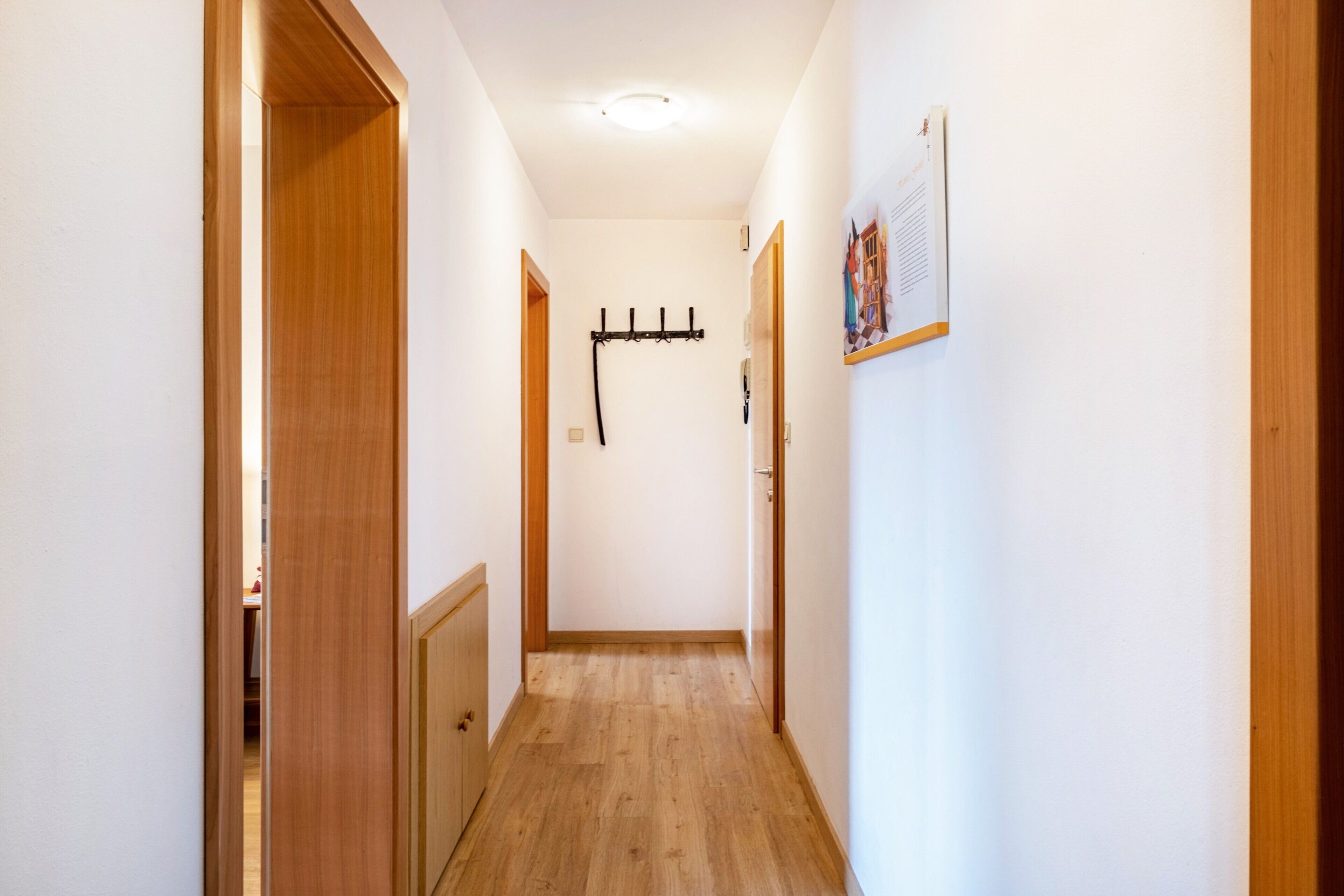 Ein schmaler Flur mit Holztüren, einem Kleiderständer und einem Korkbrett an der rechten Wand.