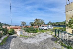 A paved road leading to a residential area with parked cars and a stone wall.