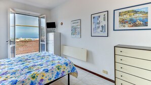 Een slaapkamer met een bed, een dressoir, een televisie en een balkon met uitzicht.