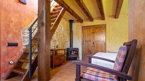 A rustic room with a wooden staircase, a bed, a chair, a fireplace, and a wooden wardrobe. - Country House "Lo Paller" with Mountain View, Shared Pool & Wi-Fi (El Perelló)