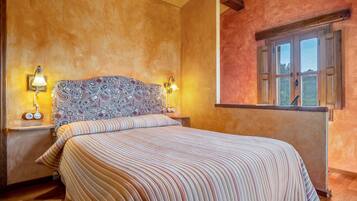 A bedroom with a large bed, patterned headboard, two bedside lamps, and a window with a view.