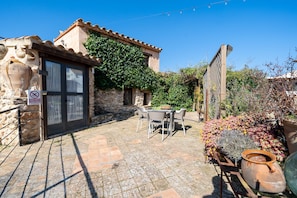 A stone building with a tiled patio, outdoor seating, and a garden with potted plants.