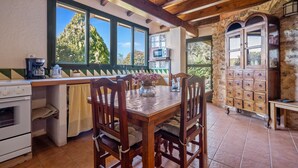 A rustic kitchen with a wooden table, chairs, a stove, and a stone wall. - Country House "Lo Paller" with Mountain View, Shared Pool & Wi-Fi (El Perelló)