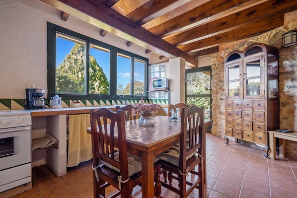 A rustic kitchen with a wooden table, chairs, a stove, and a stone wall.