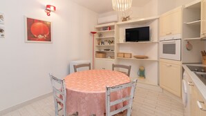 A dining area with a round table, chairs, a chandelier, a television, and kitchen cabinets. - Apartment "Palau Corallo" with Shared Garden & A/C (Palau)