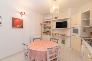 Un espace repas comprenant une table ronde, des chaises, un lustre, un téléviseur et des meubles de cuisine.