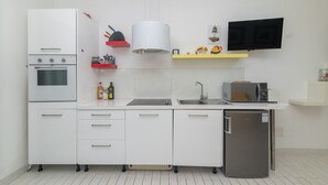 Une cuisine moderne avec des meubles blancs, un four encastré, un micro-ondes, un réfrigérateur, un évier et un luminaire suspendu.