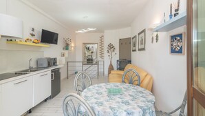 Une cuisine compacte avec un coin repas, un téléviseur fixé au mur et un petit espace de vie comprenant un canapé et des objets décoratifs.