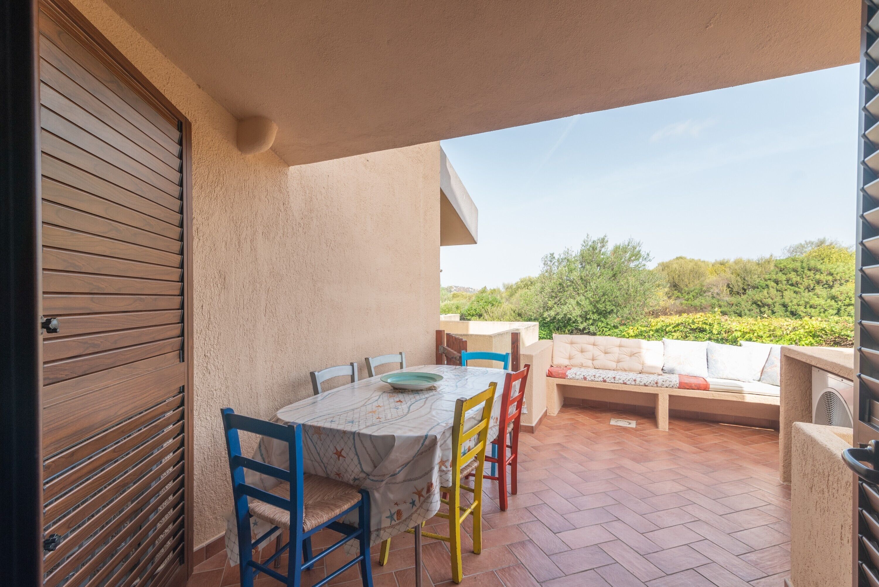 Eine Terrasse im Freien mit Tisch und Stühlen, einer gepolsterten Bank und Blick auf Grünflächen.