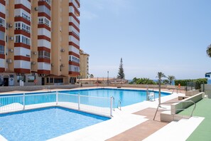 Una piscina con una cerca blanca, un edificio con franjas rojas y blancas, y un cielo despejado.