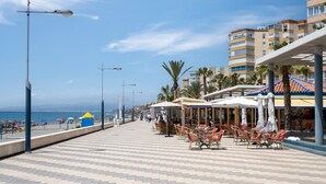 A seaside promenade with outdoor seating, a beach in the background, and a row of buildings with balconies. - Holiday Home "Beachfront Bungalow" with Sea View, Private Terrace & Wi-Fi (Torrox Costa)