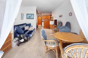 Un salón acogedor con sofá, sillas, una mesa y una cocina al fondo.