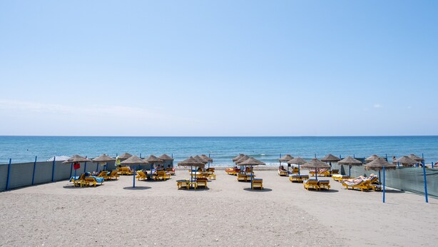 A beach with rows of sun loungers and thatched umbrellas, a sandy shore, and the sea in the background. - Holiday Home "Beachfront Bungalow" with Sea View, Private Terrace & Wi-Fi (Torrox Costa)