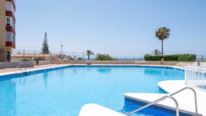 A swimming pool with clear blue water, surrounded by a white pool deck, a safety sign, and a palm tree. - Holiday Home "Beachfront Bungalow" with Sea View, Private Terrace & Wi-Fi (Torrox Costa)