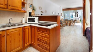 A kitchen with wooden cabinets, a microwave, and a dining area with wicker chairs. - Holiday Home "Beachfront Bungalow" with Sea View, Private Terrace & Wi-Fi (Torrox Costa)