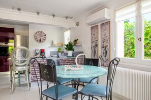 Comedor con una mesa redonda de vidrio, cuatro sillas, un reloj, pared de ladrillo y una ventana con follaje exterior.