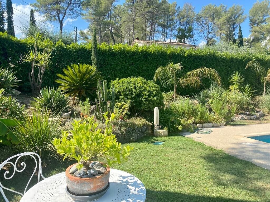 Un jardin bien entretenu, agrémenté de diverses plantes, d’un banc en pierre et offrant une vue dégagée sur une piscine.