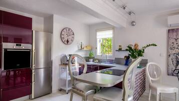 A modern kitchen with stainless steel appliances, a dining table with chairs, and a decorative clock on the wall.