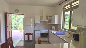 Eine kleine Küche mit Kühlschrank, Herd, Spüle und Schränken. Ein Fenster sorgt für natürliches Licht, und eine Tür führt nach draußen.