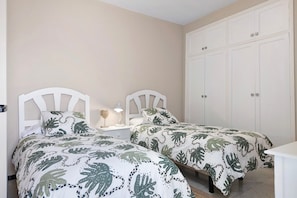 A bedroom with two beds, a nightstand with a lamp, and a wardrobe.