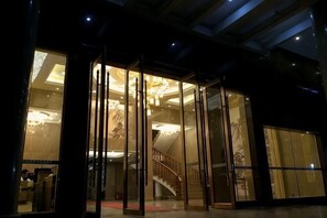 Een hotelentree met een glazen deur, een trap en een kroonluchter.