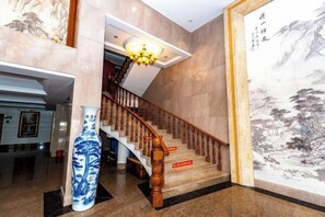 A staircase with a wooden handrail, a vase, and a large painting on the wall. - Xingchen Haitian Resort (Taishan)