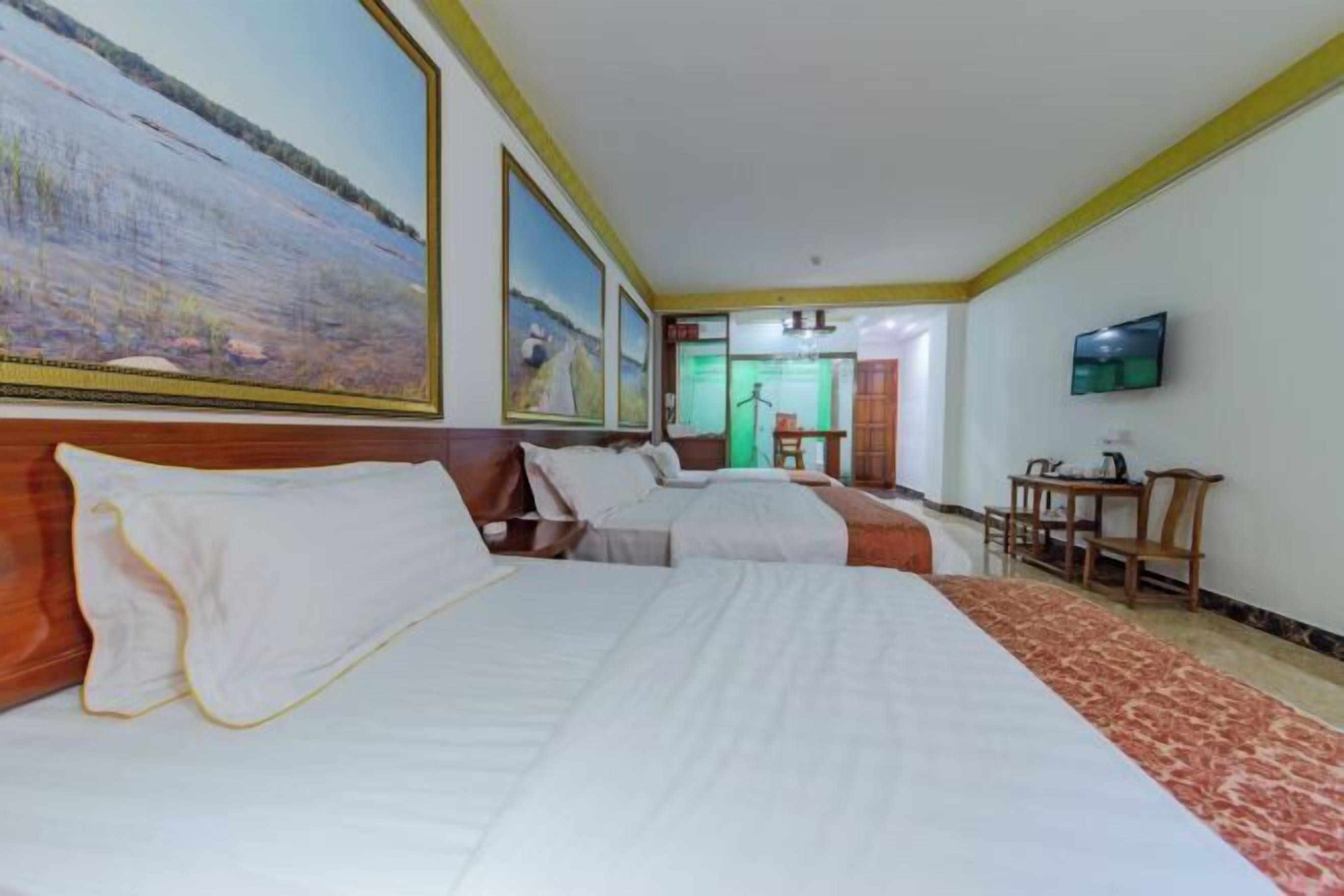 A hotel room with two beds, a television, a desk, and a large painting on the wall.