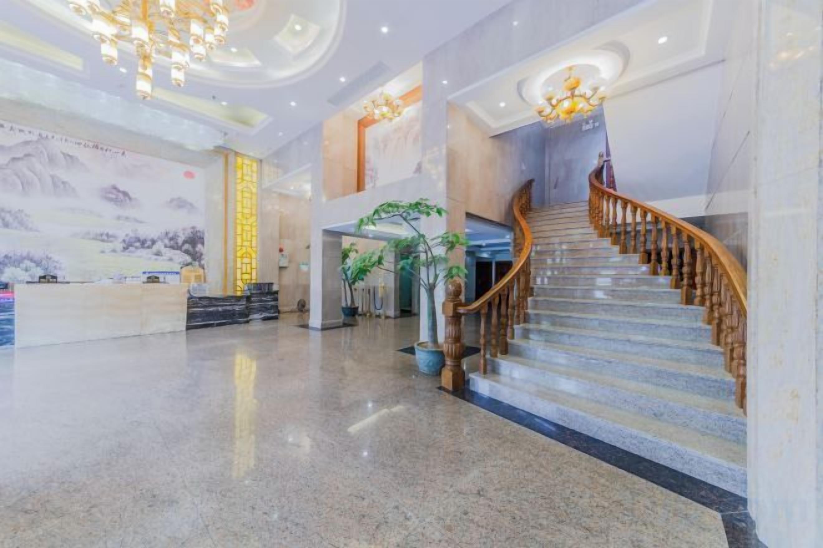 Un'ampia hall con pavimento in marmo, una reception, una scala con ringhiere in legno e un grande lampadario.