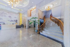 A spacious lobby with a marble floor, a reception desk, a staircase with wooden railings, and a large chandelier. - Xingchen Haitian Resort (Taishan)