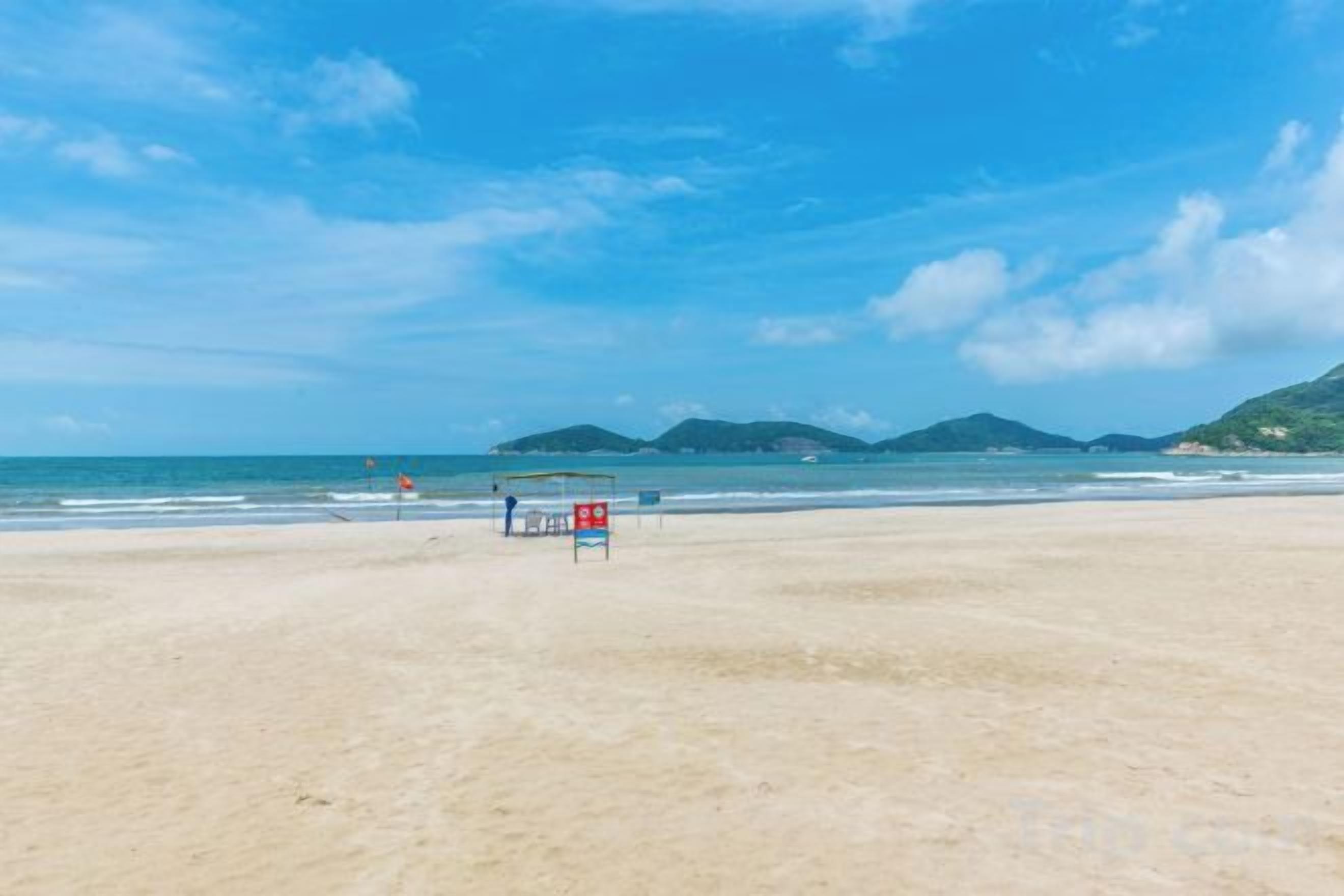 Une plage avec un poste de surveillance pour les sauveteurs, un ciel dégagé et des montagnes à l’horizon.