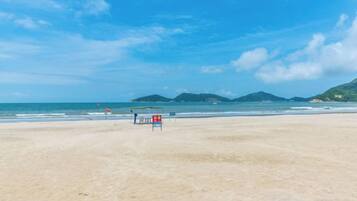 Une plage avec un poste de surveillance pour les sauveteurs, un ciel dégagé et des montagnes à l’horizon.