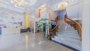 Eine großzügige Lobby mit Marmorboden, einer Holztreppe und einem Empfangsbereich.