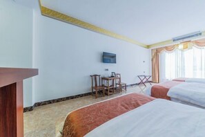 Ein Hotelzimmer mit zwei Betten, einem Schreibtisch mit Stühlen, einem Flachbildfernseher und einem Fenster mit Vorhängen.