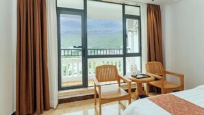 Ein Hotelzimmer mit Bett, zwei Holzstühlen, einem kleinen Tisch und einem Balkon mit Blick auf die Hügel.