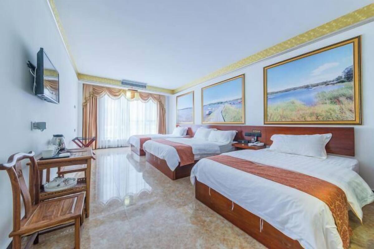 A hotel room with three beds, a wooden desk, and a television.
