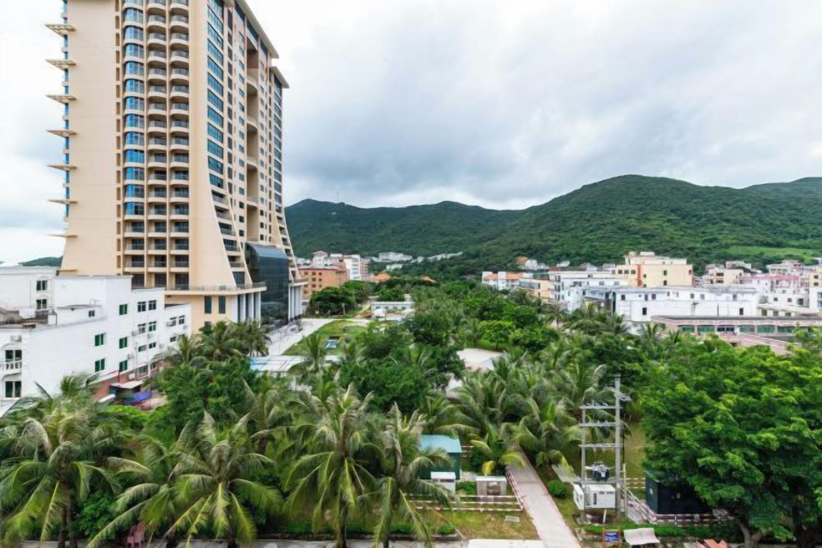 A high-rise building with multiple floors, surrounded by greenery and other buildings.