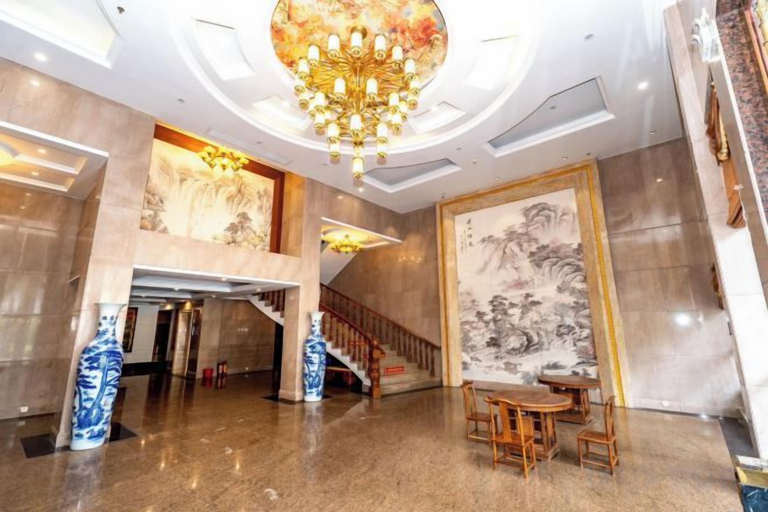 A spacious lobby with a grand chandelier, a staircase, and traditional artwork.
