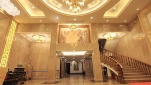 Eine geräumige Lobby mit einer imposanten Treppe, einem Chandelier und einem großen Wandgemälde.