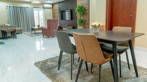 A modern dining area with a dark wooden table, grey and brown chairs, a small side table, and a potted plant. - Integral Consults Apartment (Abuja)