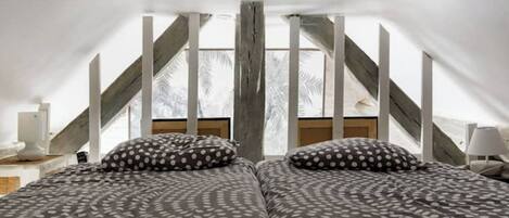 Un dormitorio con dos camas, cada una con ropa de cama de lunares, techo de madera y vistas a palmeras a través de amplias ventanas.