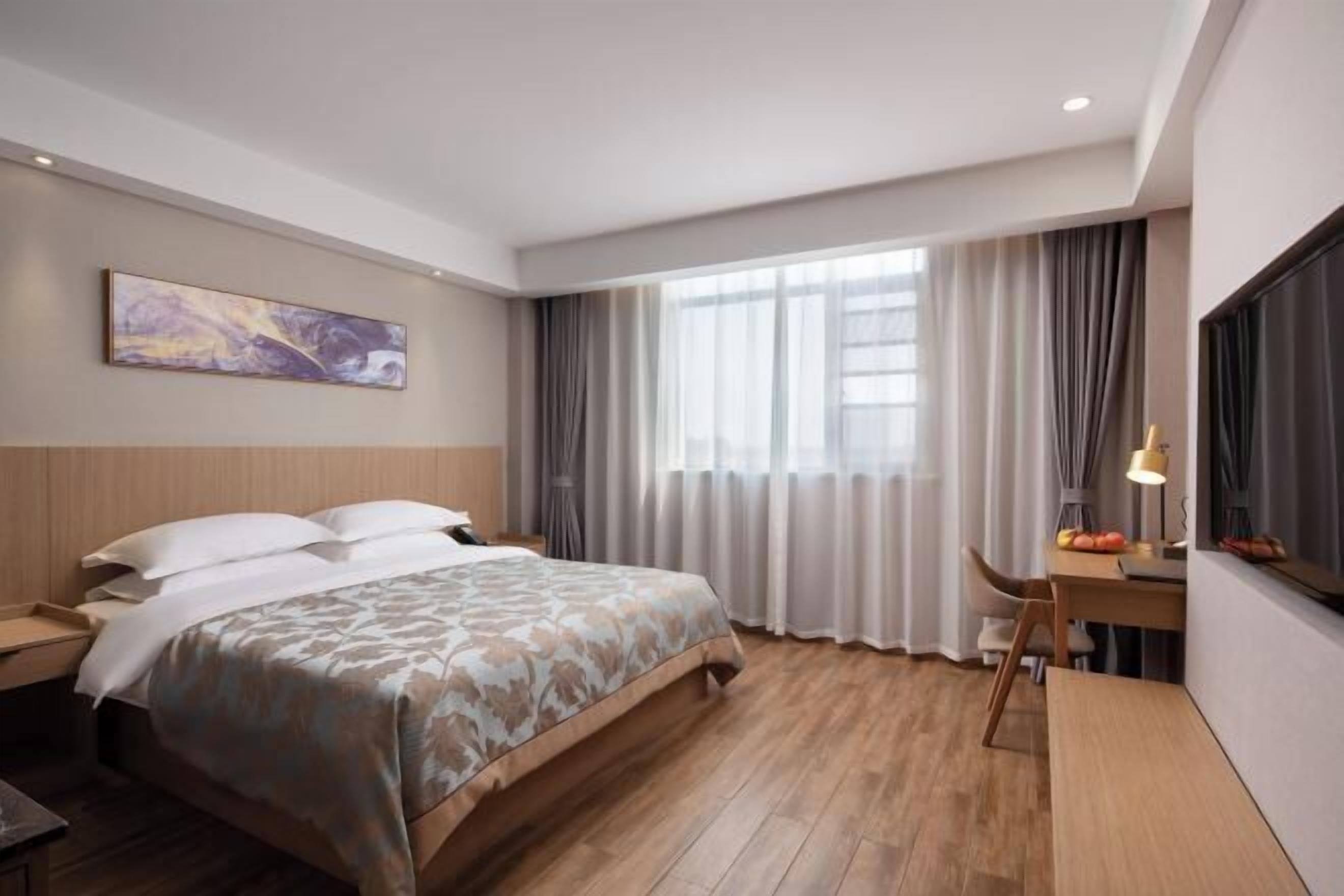 A hotel room with a bed, a desk, a chair, a lamp, and a painting on the wall.