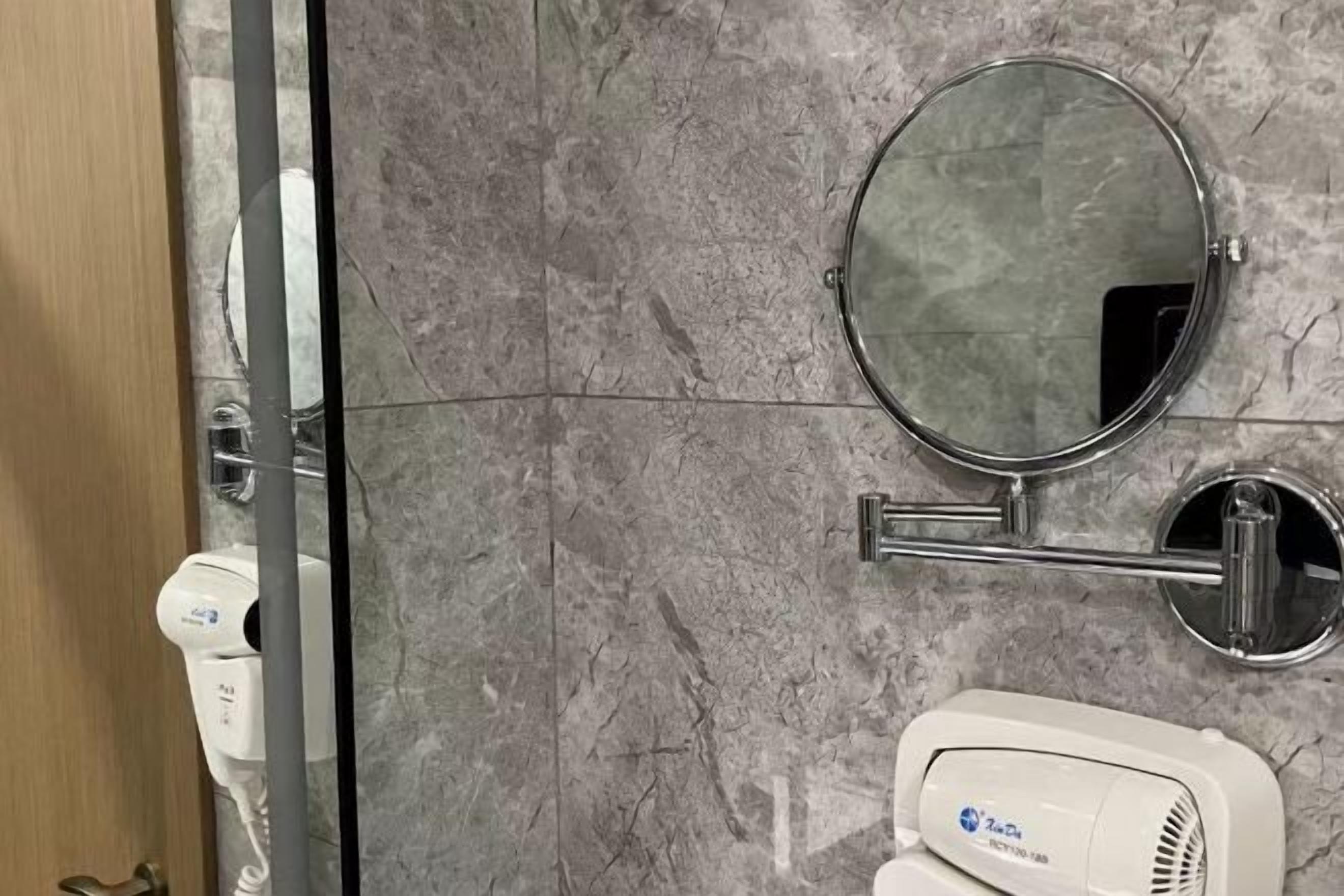 Une salle de bain avec un mur en marbre, un miroir rond, un porte-serviettes et un sèche-cheveux.