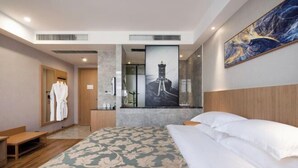 Hotelkamer met een groot bed, een houten hoofdbord, een schilderij aan de muur en een badkamer achter een glazen wand.