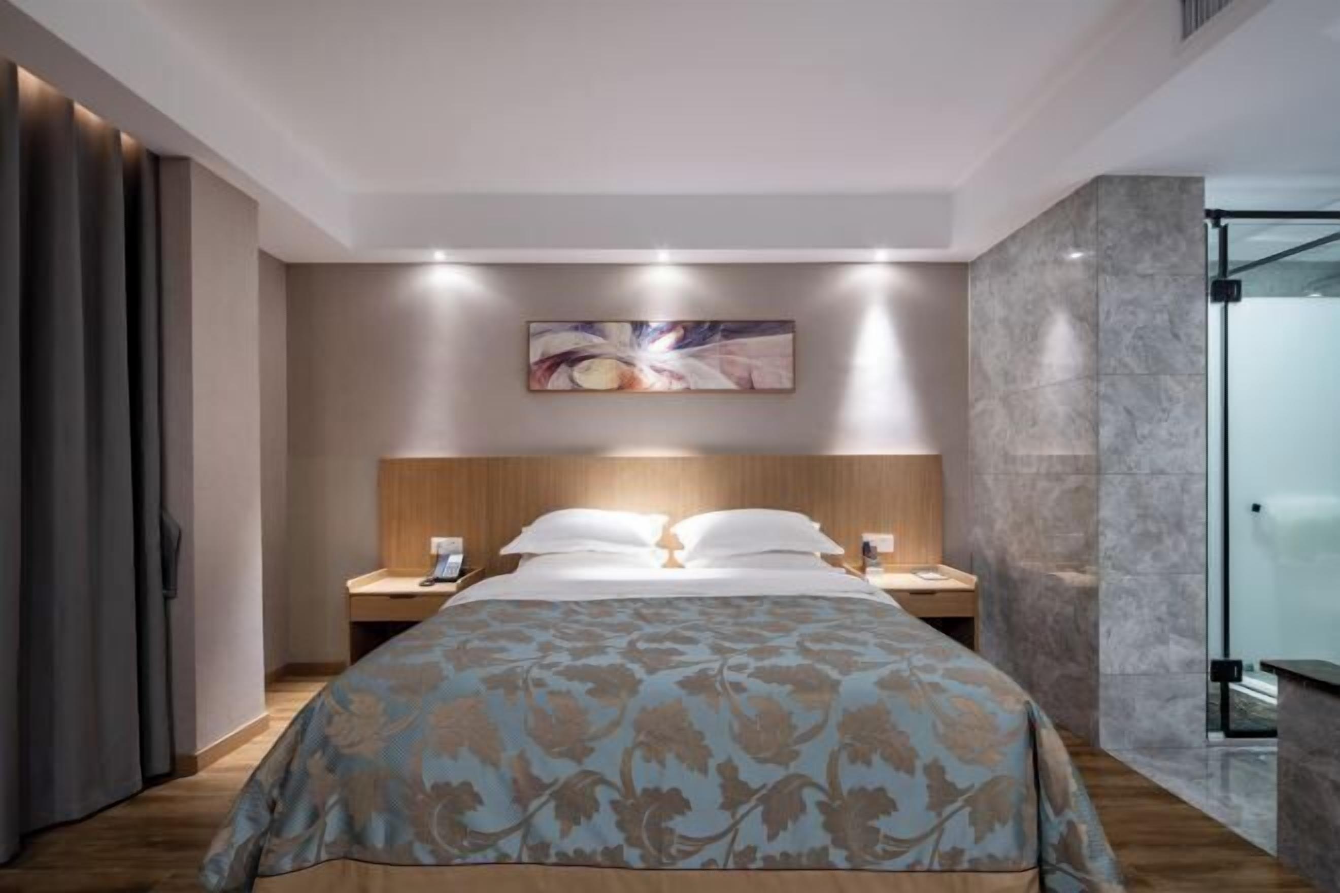 Een moderne hotelkamer met een groot bed, een houten hoofdeinde, een nachtkastje en een douchecabine met glazen wanden.