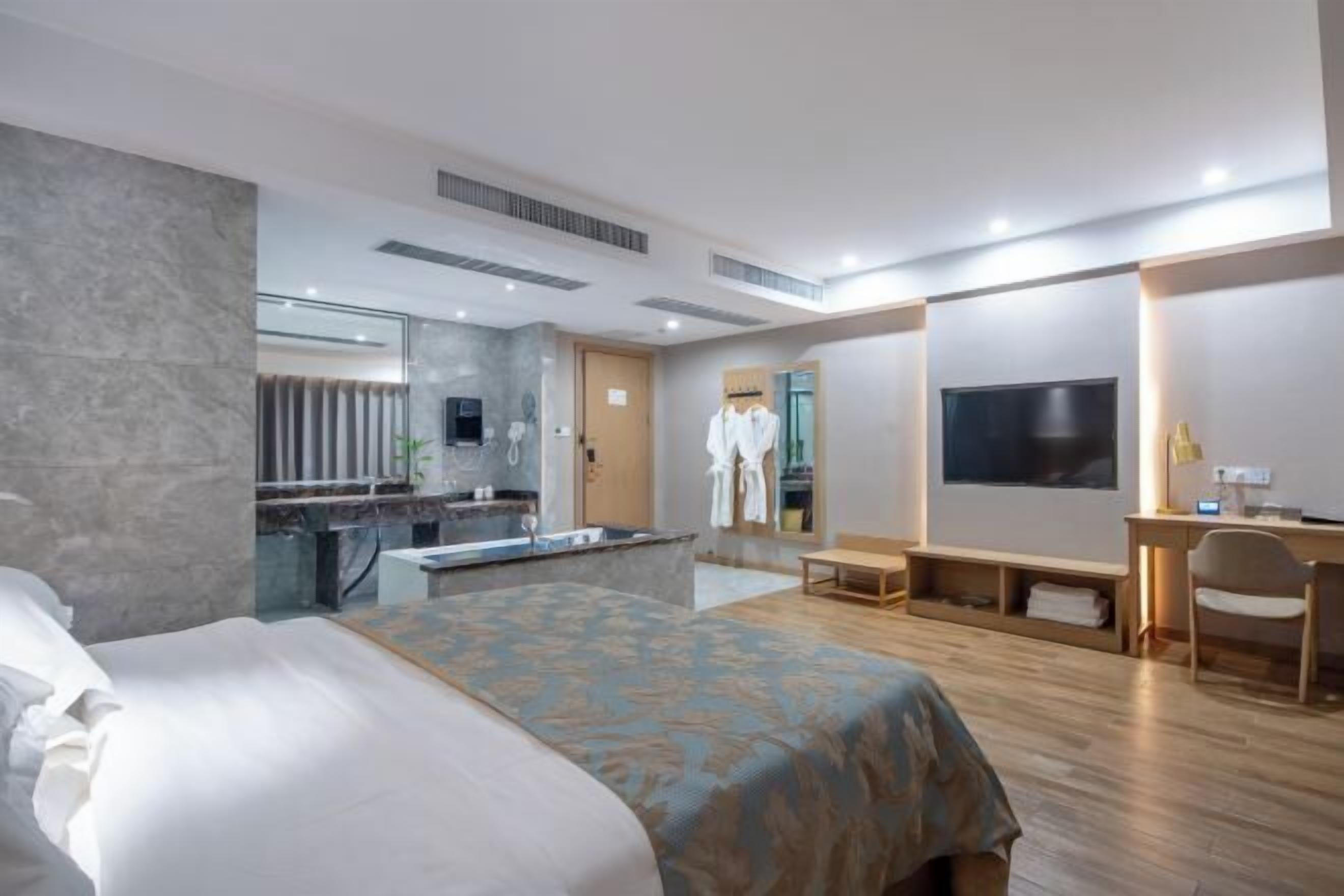 A hotel room with a bed, a desk, a TV, and a bathroom with a mirror and towel rack.