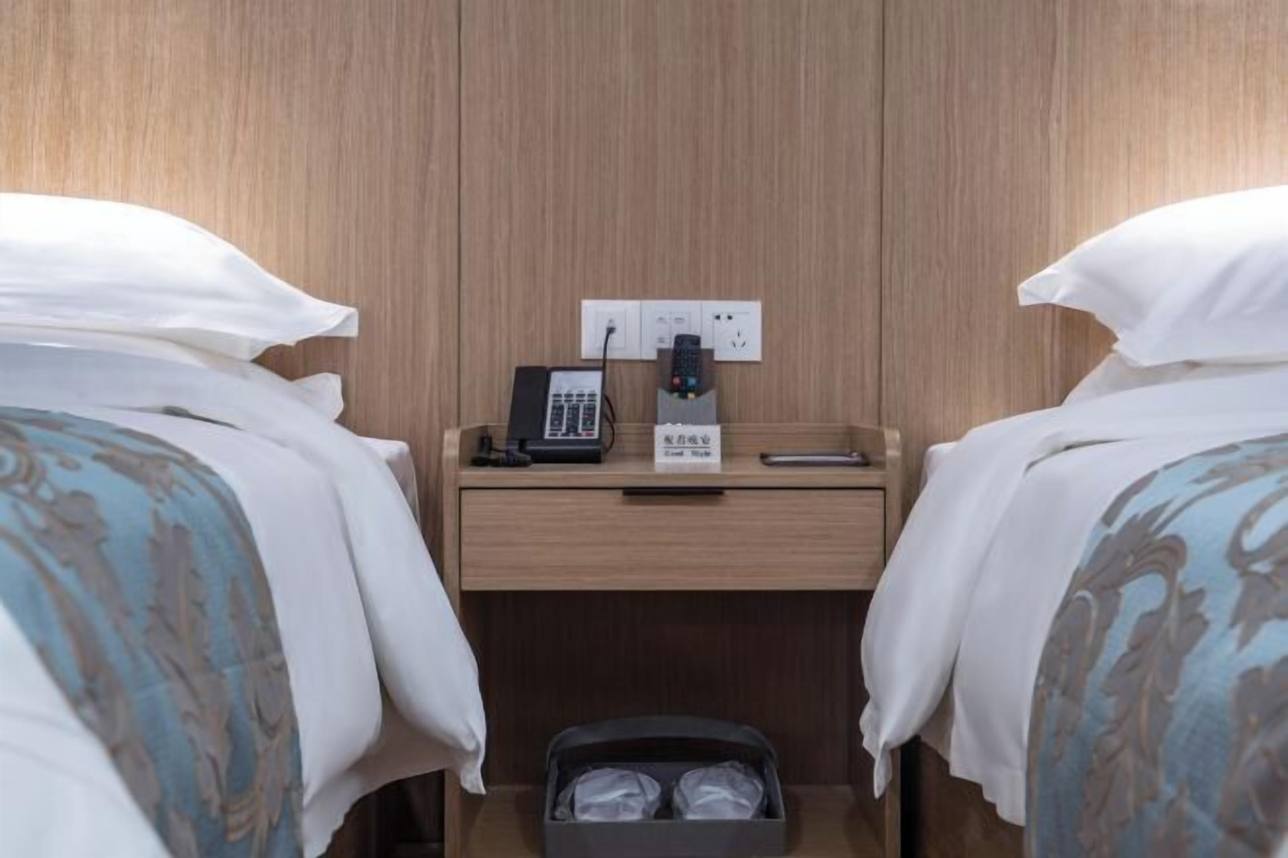 Une chambre d’hôtel avec deux lits, une table de chevet avec un téléphone et une télécommande, et un petit coffre de rangement.
