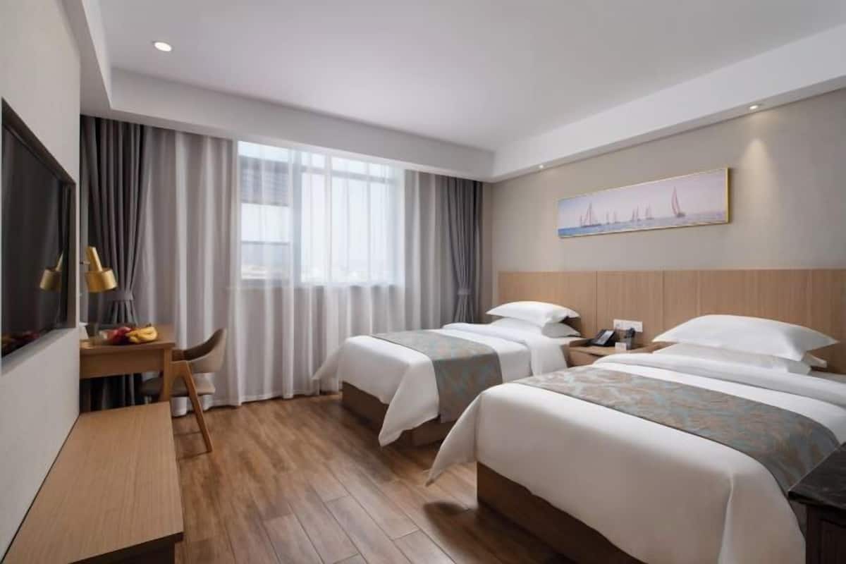 Ein Hotelzimmer mit zwei Betten, einem Schreibtisch, einem Stuhl und einem Bild an der Wand.