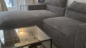 A modern living room with a sectional sofa, a glass coffee table, and a wall-mounted TV. - Superb apartment for rent (Paris)