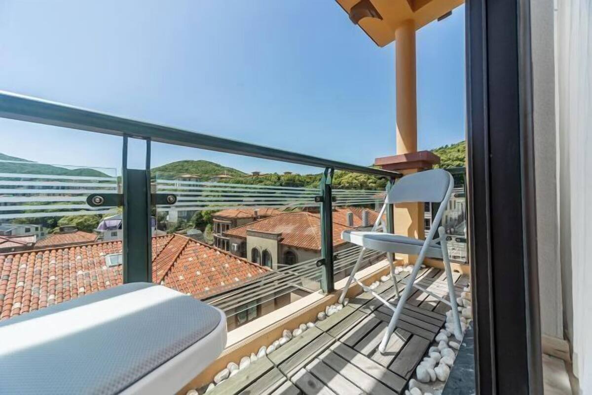 A balcony with a view of a cityscape, including buildings with red-tiled roofs and a distant bridge.